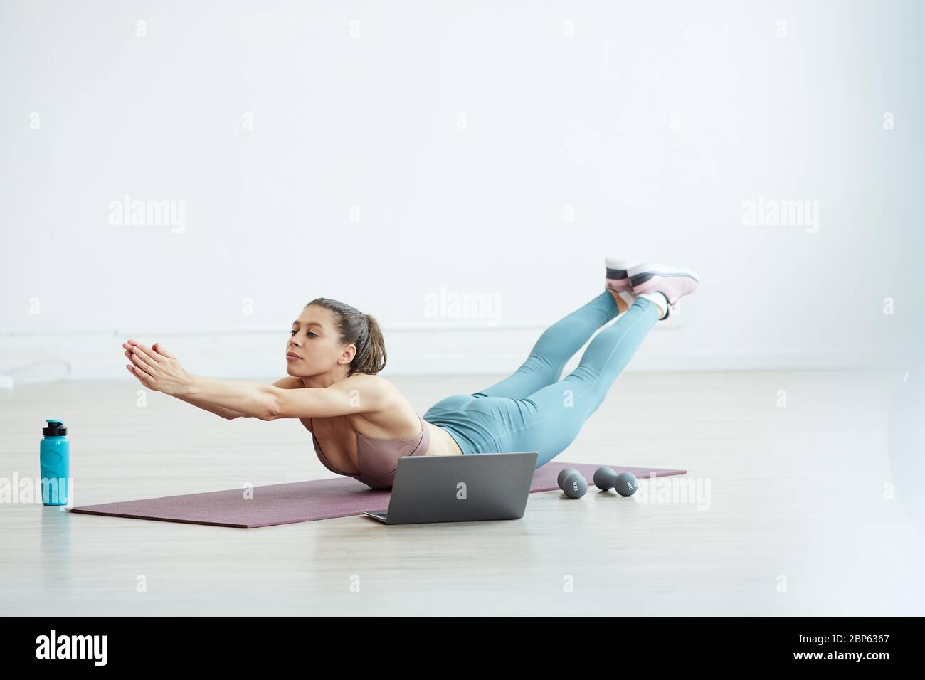 Minimal full length portrait of fit young woman stretching on yoga mat ...