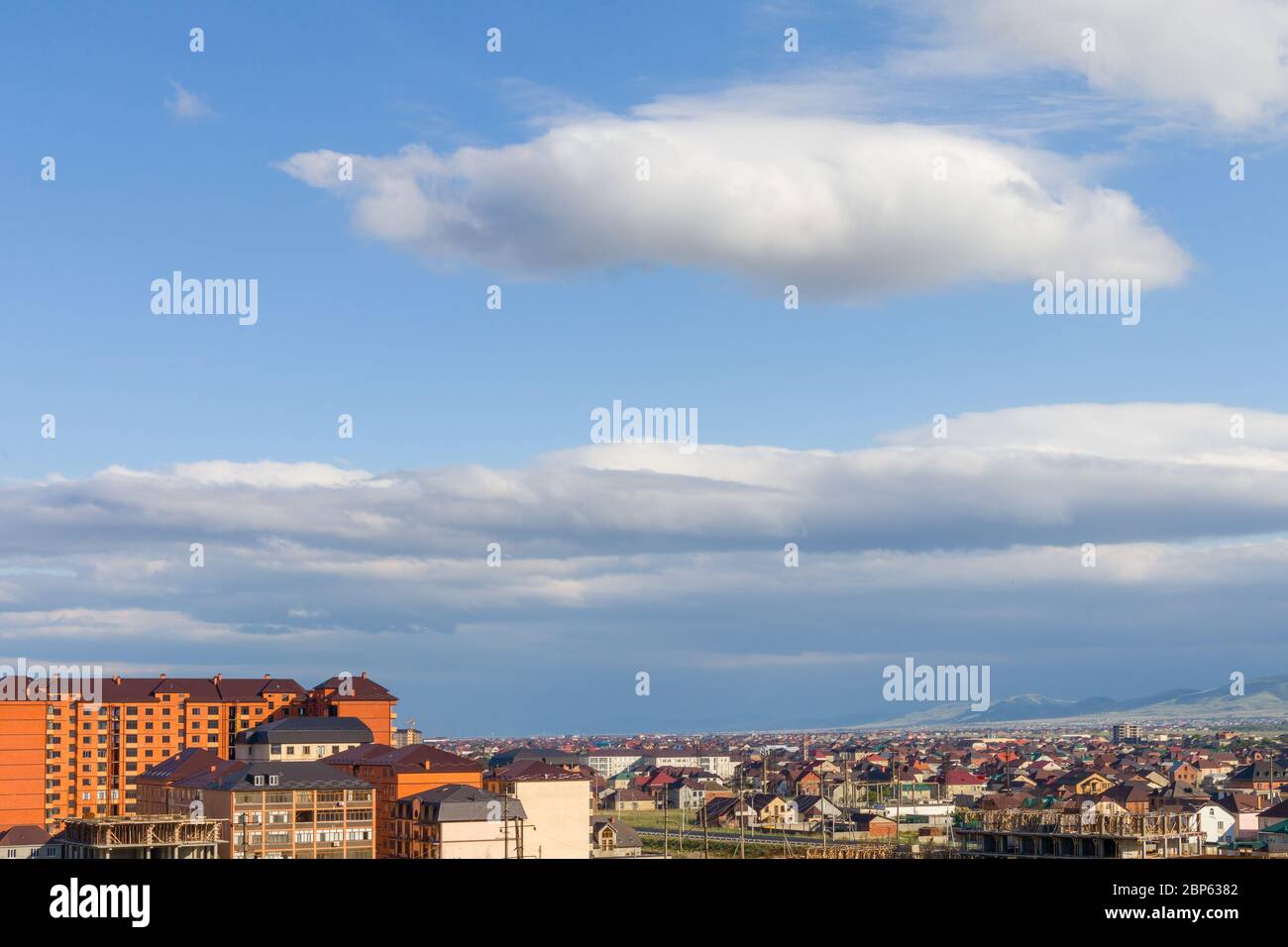 White clouds on the blue clean sky with sun rays above a city.  Stock Photo