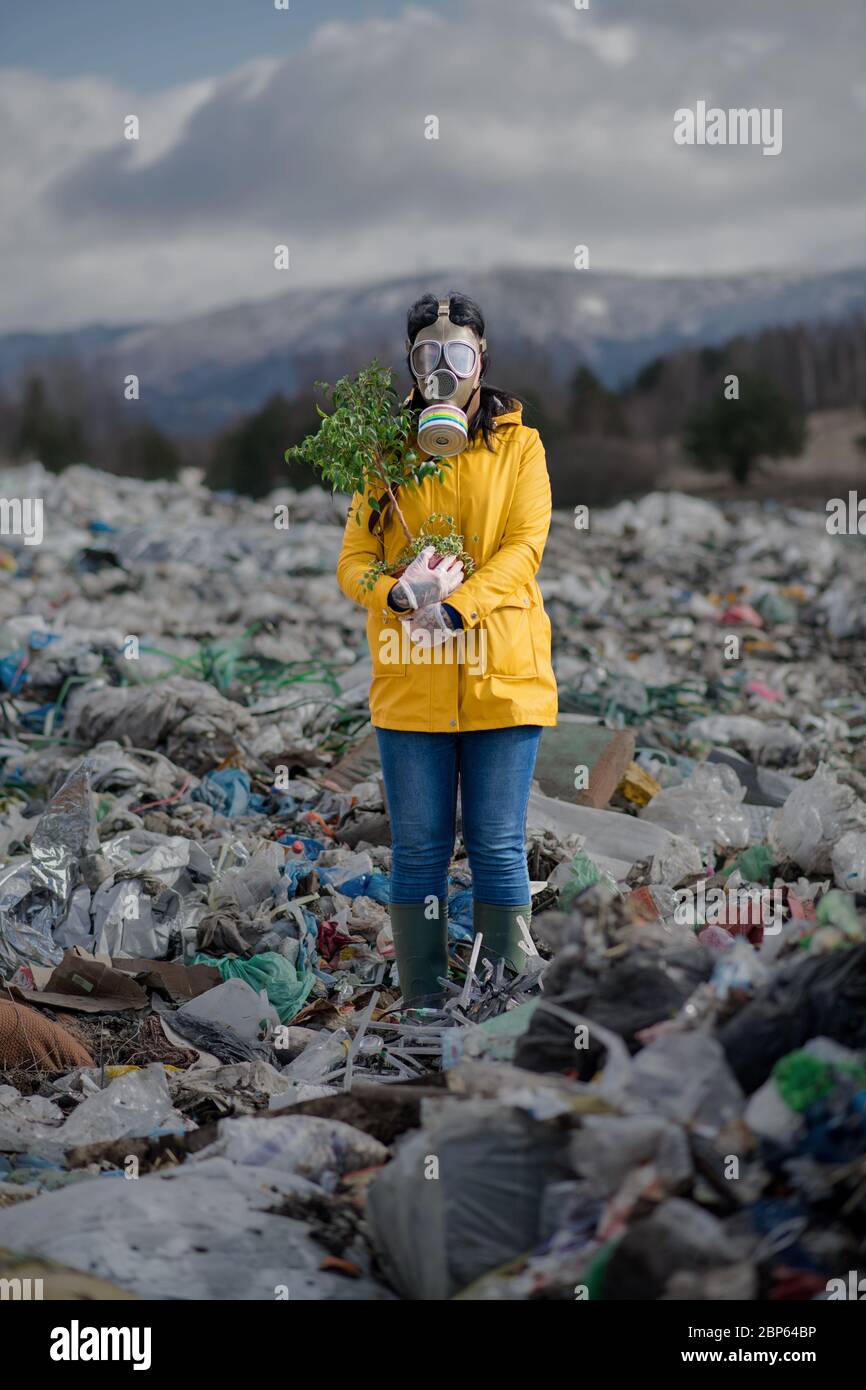 Woman with gas mask holding green plant on landfill, environmental concept. Stock Photo
