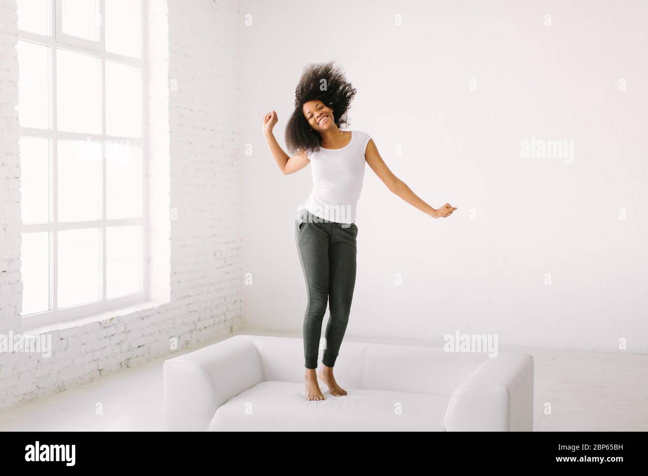 An African American young woman jumping on white bed Stock Photo - Alamy