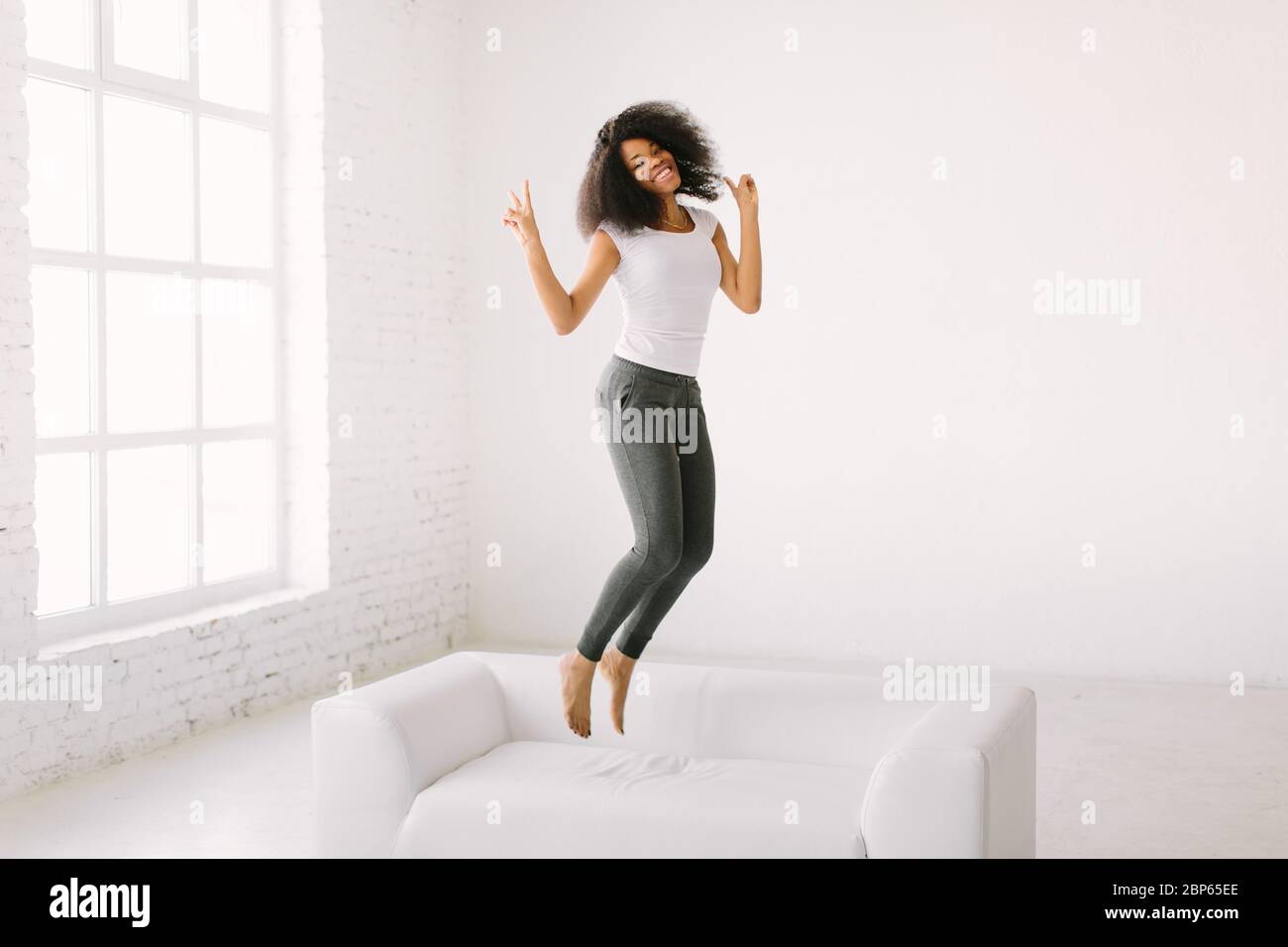 An African American young woman jumping on white bed Stock Photo - Alamy