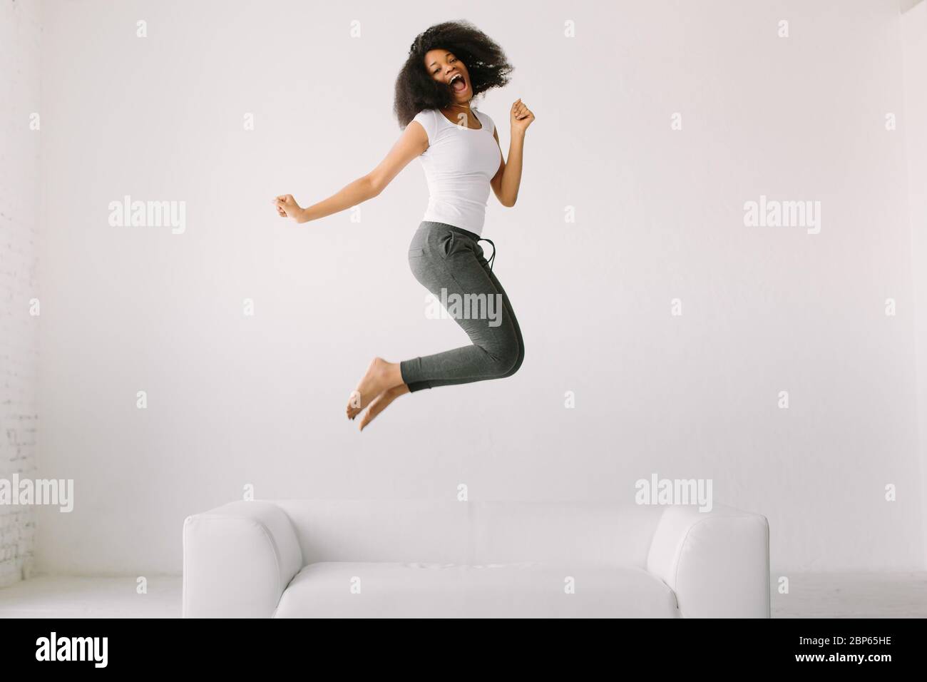 An African American young woman jumping on white bed Stock Photo - Alamy
