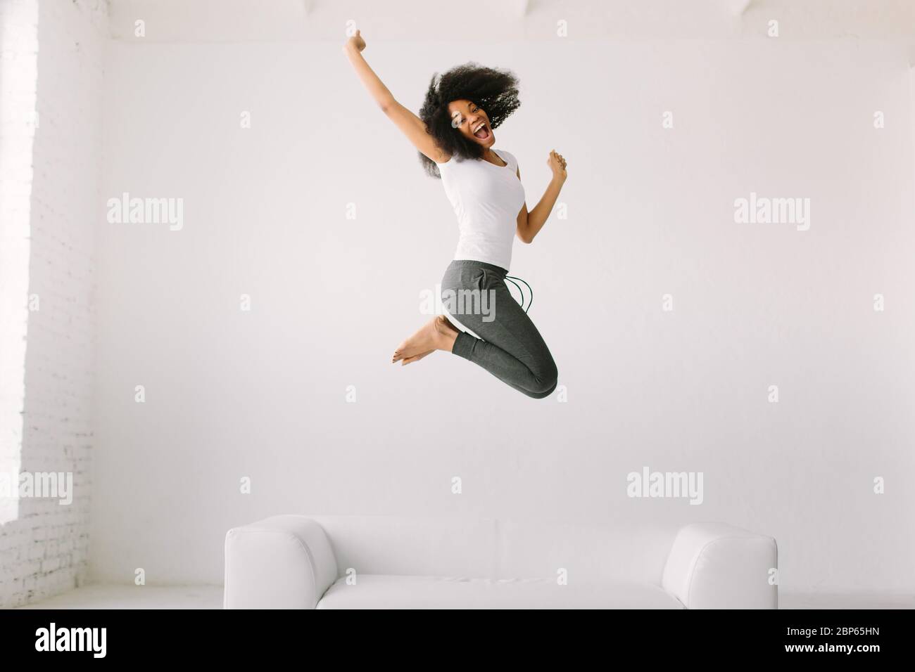 An African American young woman jumping on white bed Stock Photo - Alamy