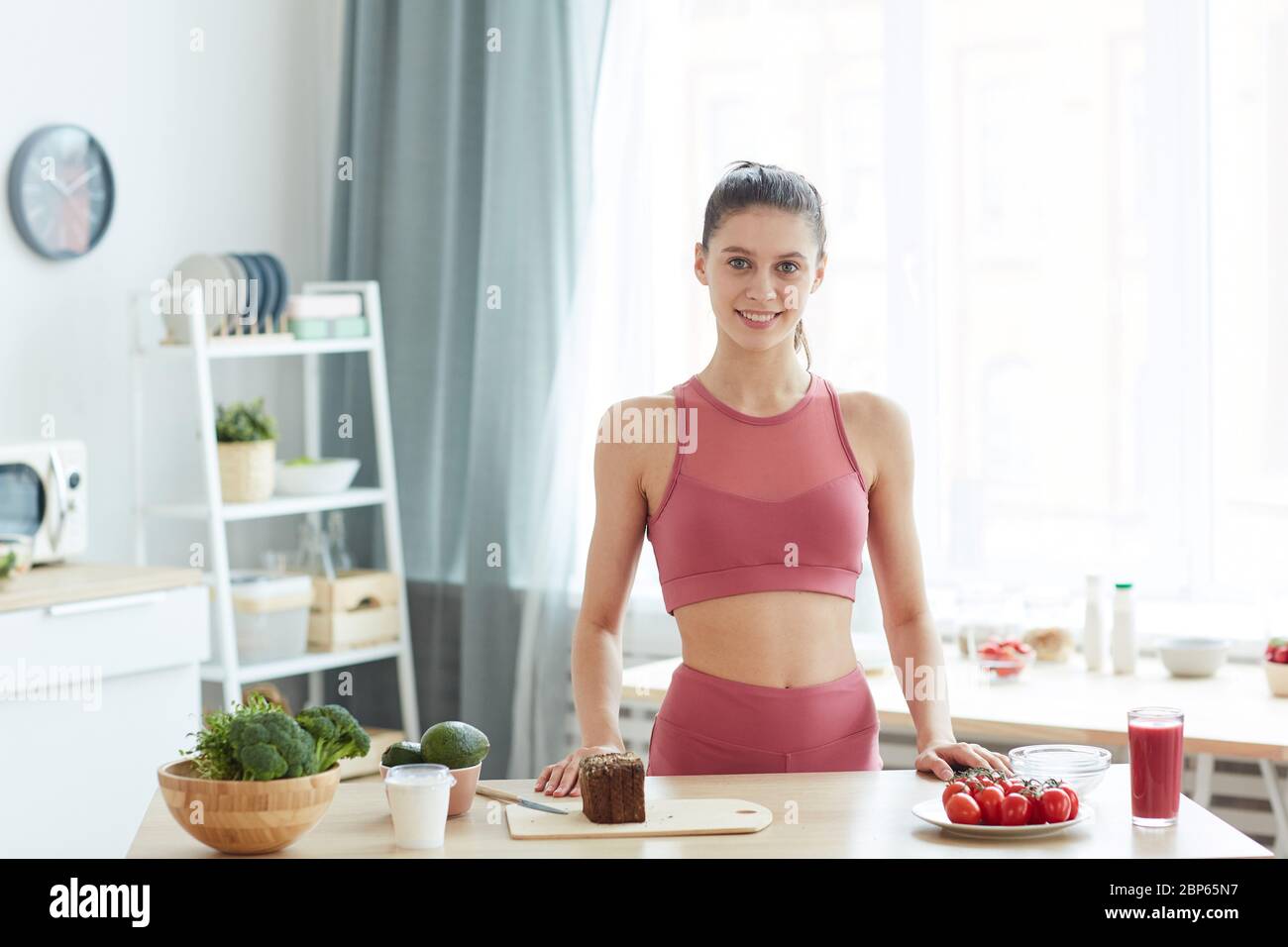 Waist up portrait of fit young woman cooking healthy food in kitchen interior and smiling at camera, copy space Stock Photo