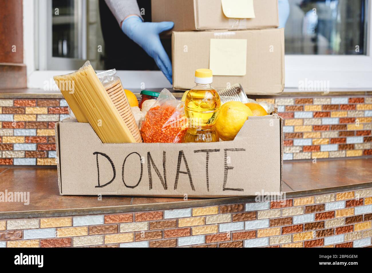 Donation box with food on doorstep near home door. Delivery mail boxes in female hands. Woman in protective gloves holding Delivery box. Contactless Stock Photo