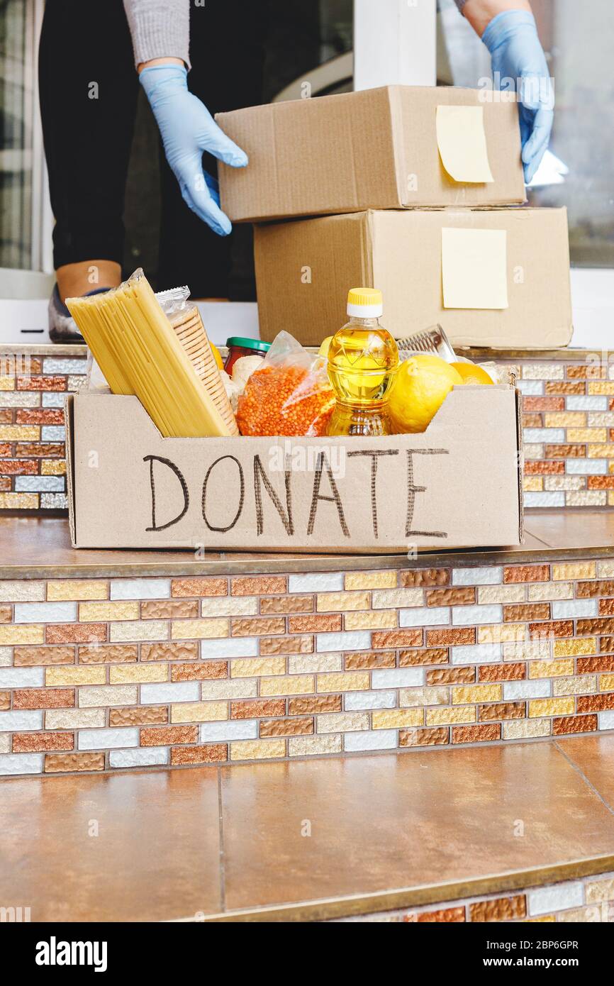 Donation box with food on doorstep near home door. Delivery mail boxes in female hands. Woman in protective gloves holding Delivery donate box,covid Stock Photo