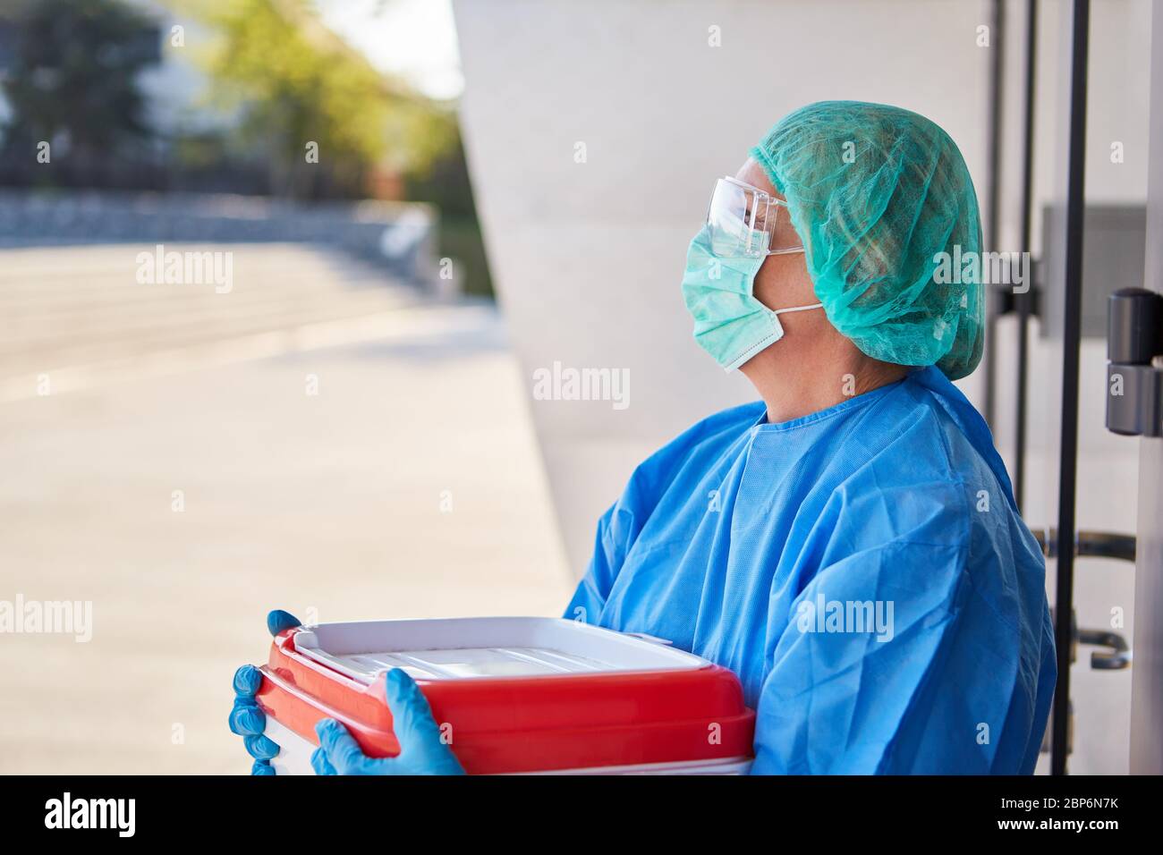 Doctor or surgeon in organ transport for surgery in front of the clinic in protective clothing pauses at the door Stock Photo