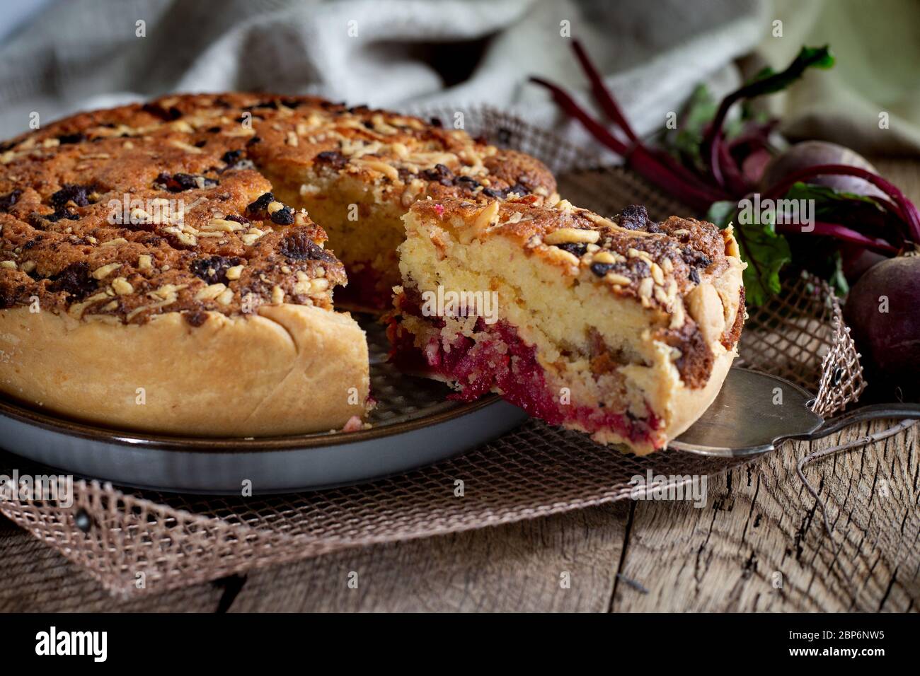 Homemade delicious beetroot pastry tart on kitchen grill with slice of cake and fresh beetroots on rustic wooden bakground. Menu, board, banner. Vintage traditional rustic kitchen. British meal Stock Photo