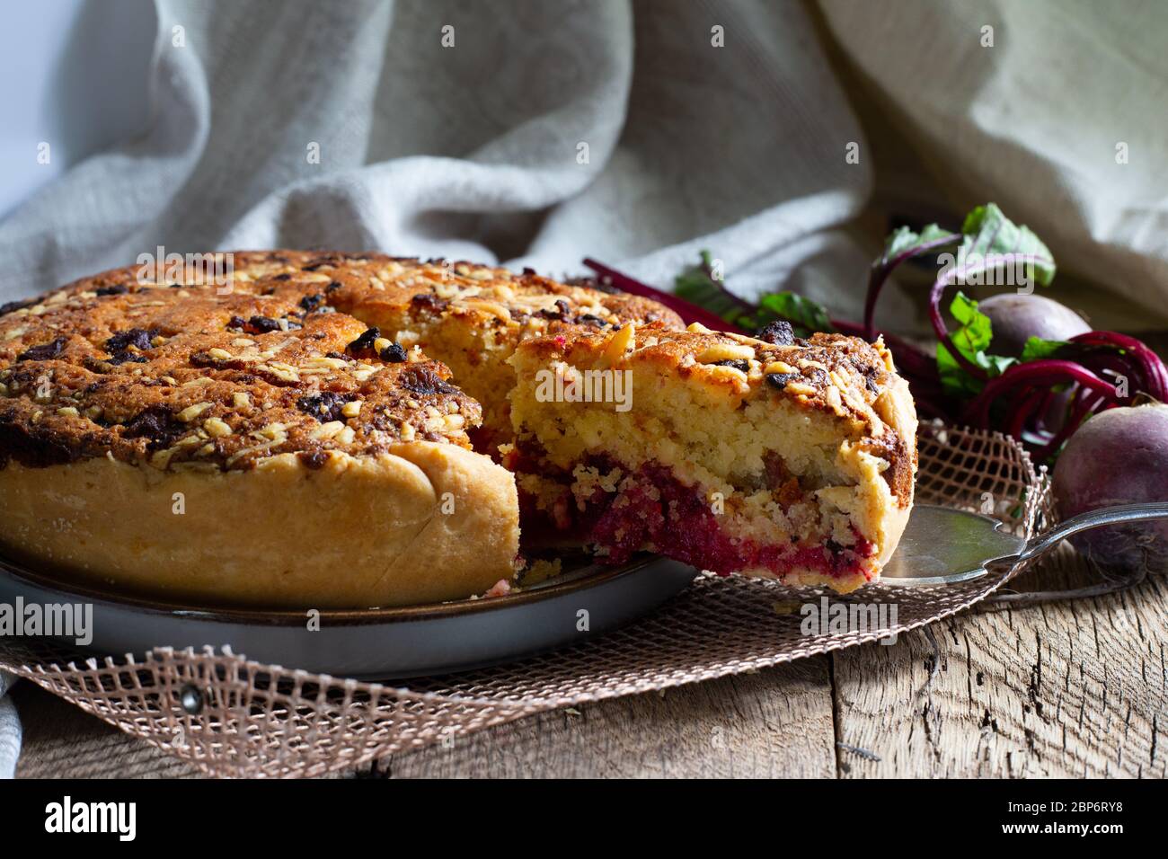 Homemade delicious beetroot pastry tart on kitchen grill with slice of cake and fresh beetroots on rustic wooden bakground. Menu, board, banner. Vintage traditional rustic kitchen. British meal Stock Photo