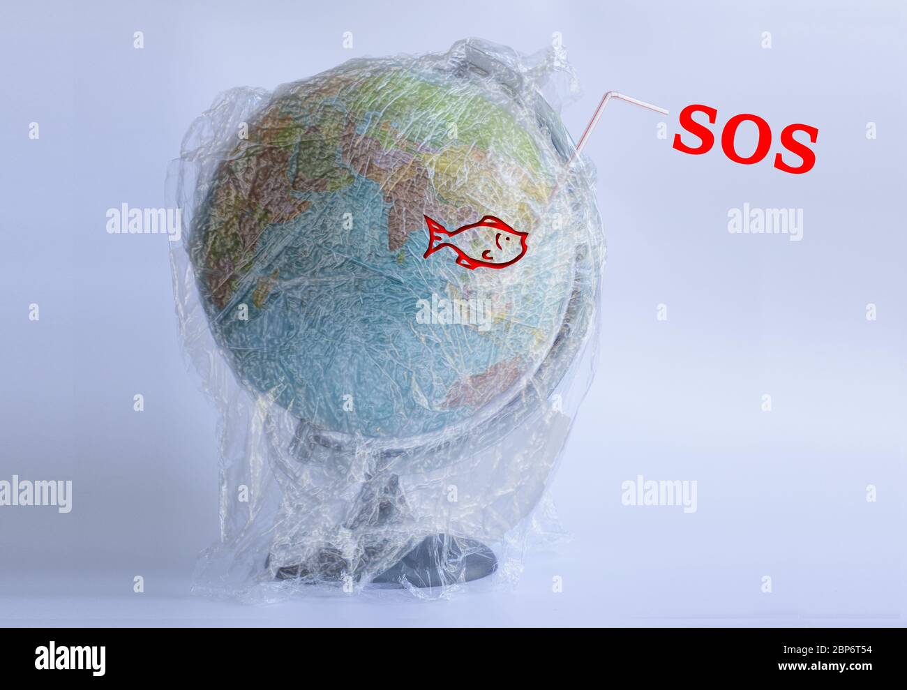 Text SOS and icon of fish on the Model planet Earth in polyethylene plastic disposable package on light grey background. Ecology problems. Concept pollution of environment with polyethylene plastic waste. World Earth Day. Save the planet Stock Photo