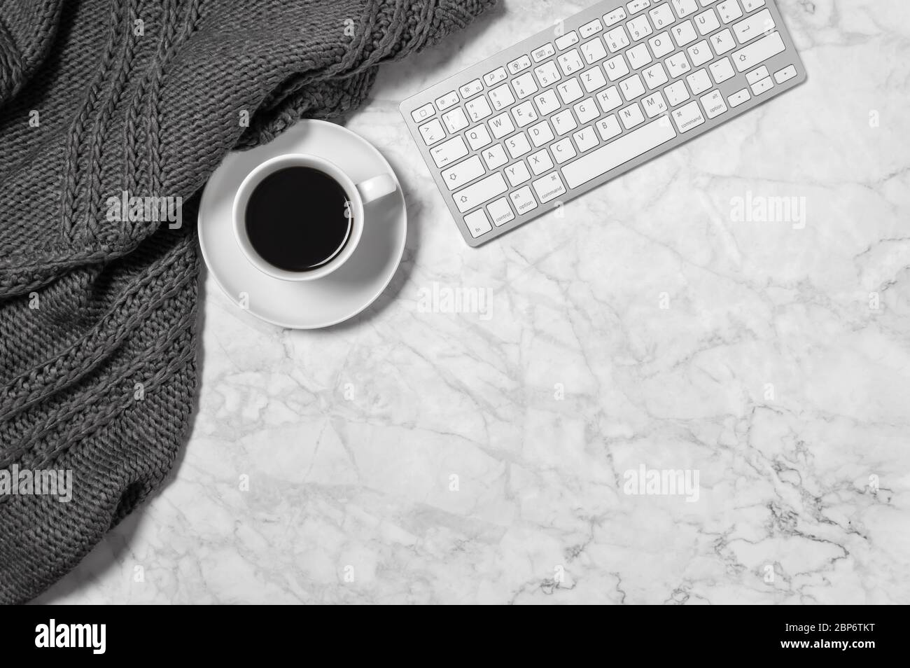Marble desk with warm wool plaid or scarf, coffee cup and keyboard in black and white. Cozy home office workspace. Minimalist freelance or business co Stock Photo