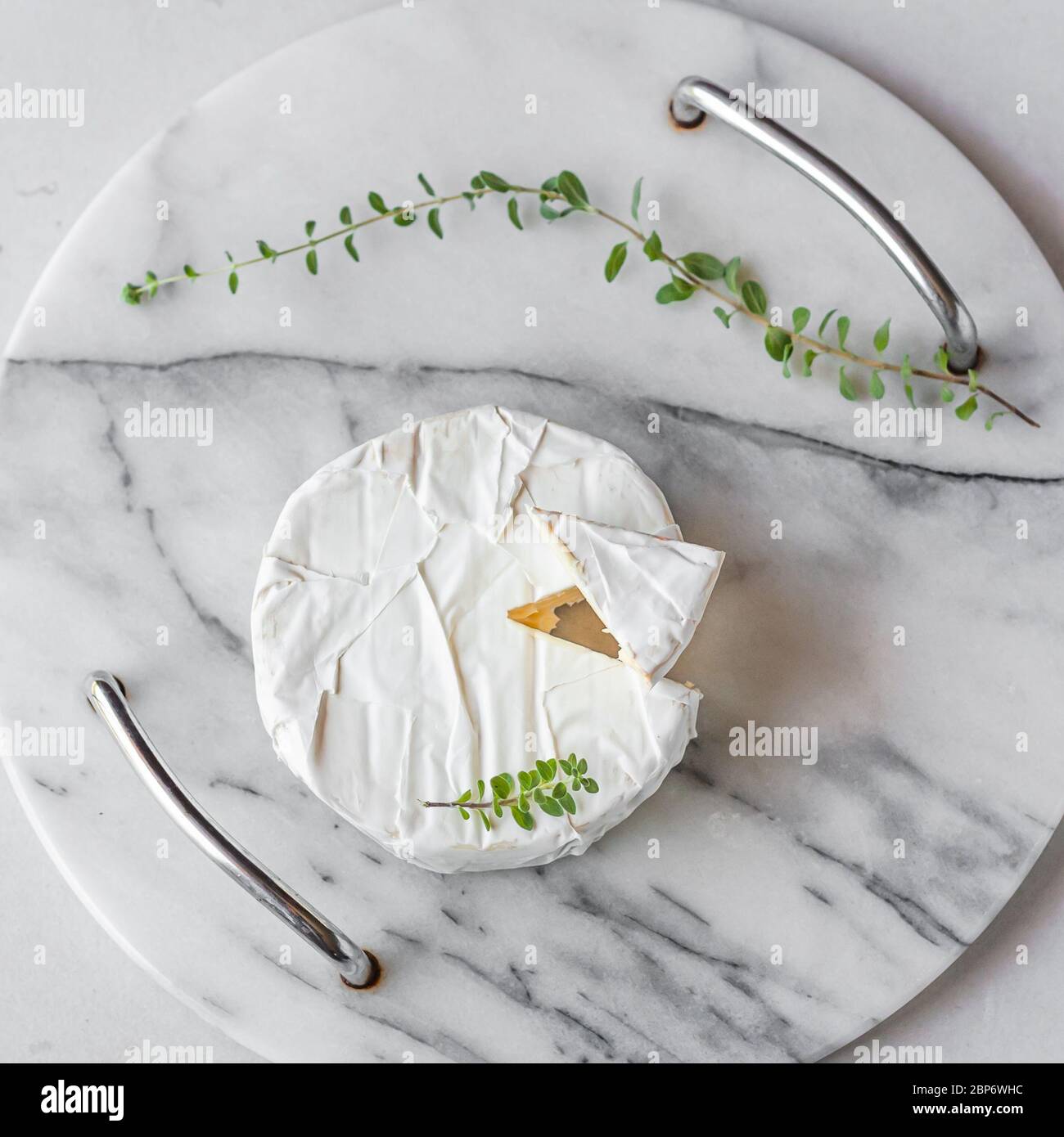 Round Brie cheese with a section cut out on a marble tray on white