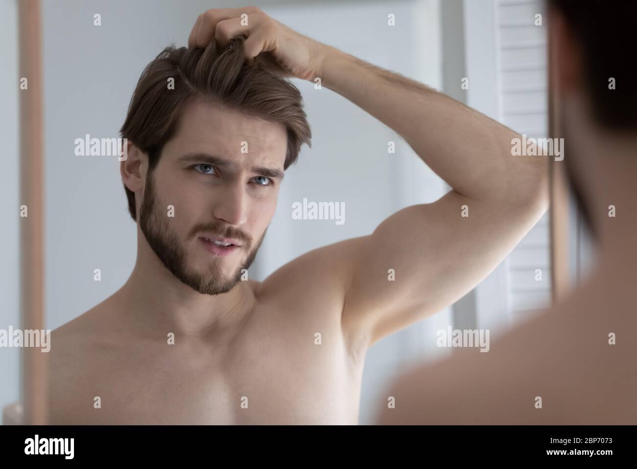 Unhappy young man look in mirror worried about hair loss Stock Photo