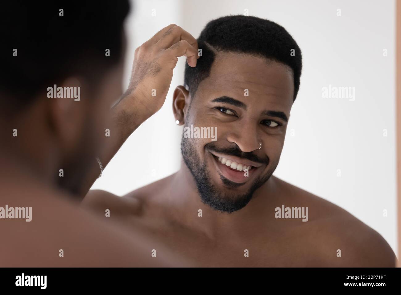 Smiling african American man look in mirror in bathroom Stock Photo