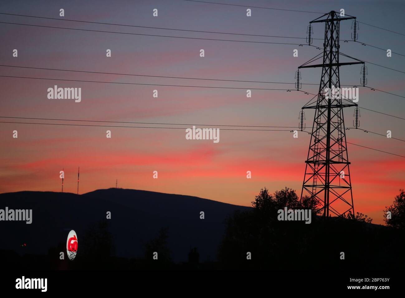A electricity pylon, along with Cavehill mountain, forms a silhouette as the sun goes down over east Belfast in Northern Ireland. Stock Photo