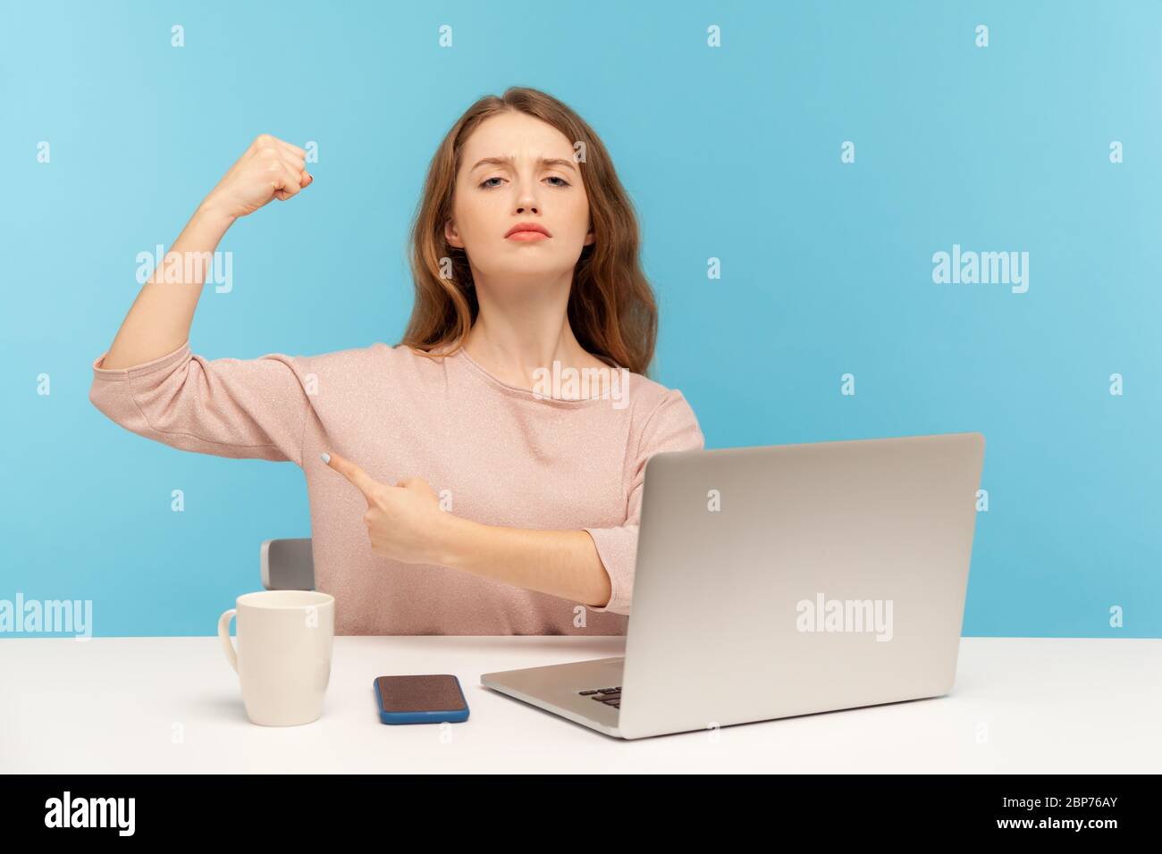 Independent strong confident woman boss sitting at workplace with laptop and showing biceps, looking proud, feeling power to success in business. indo Stock Photo