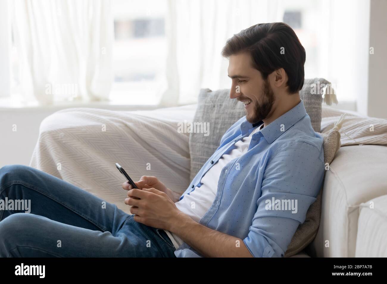 Smiling man rest on couch using smartphone gadget Stock Photo