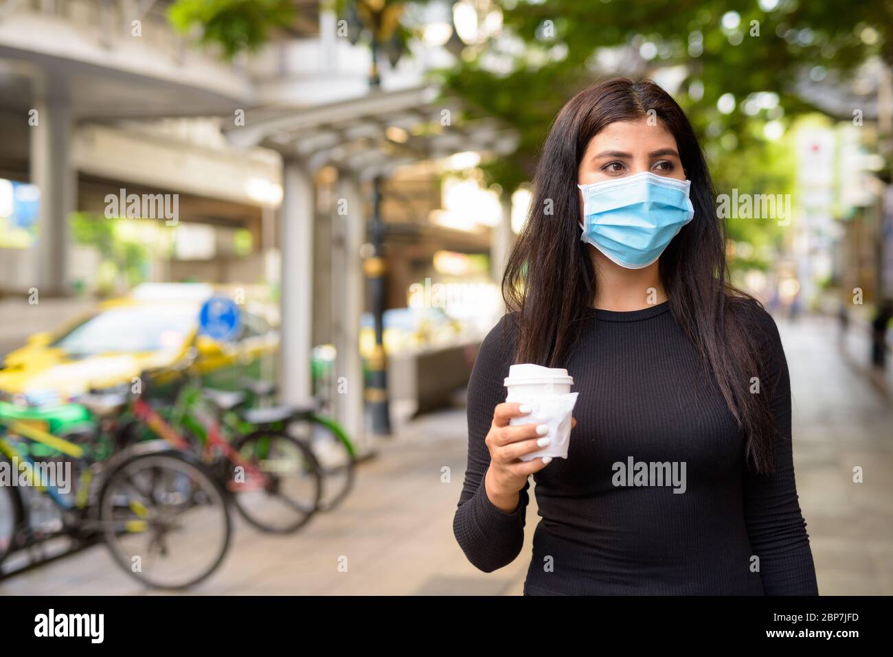 Young Indian woman with mask having coffee on the go as the new normal during covid-19 in the city Stock Photo