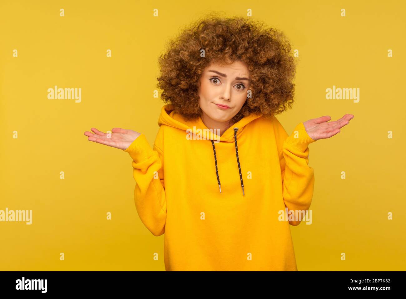 Don't know, sorry. Portrait of clueless uncertain confused curly-haired woman in urban style hoodie shrugging shoulders in questioning gesture, lookin Stock Photo