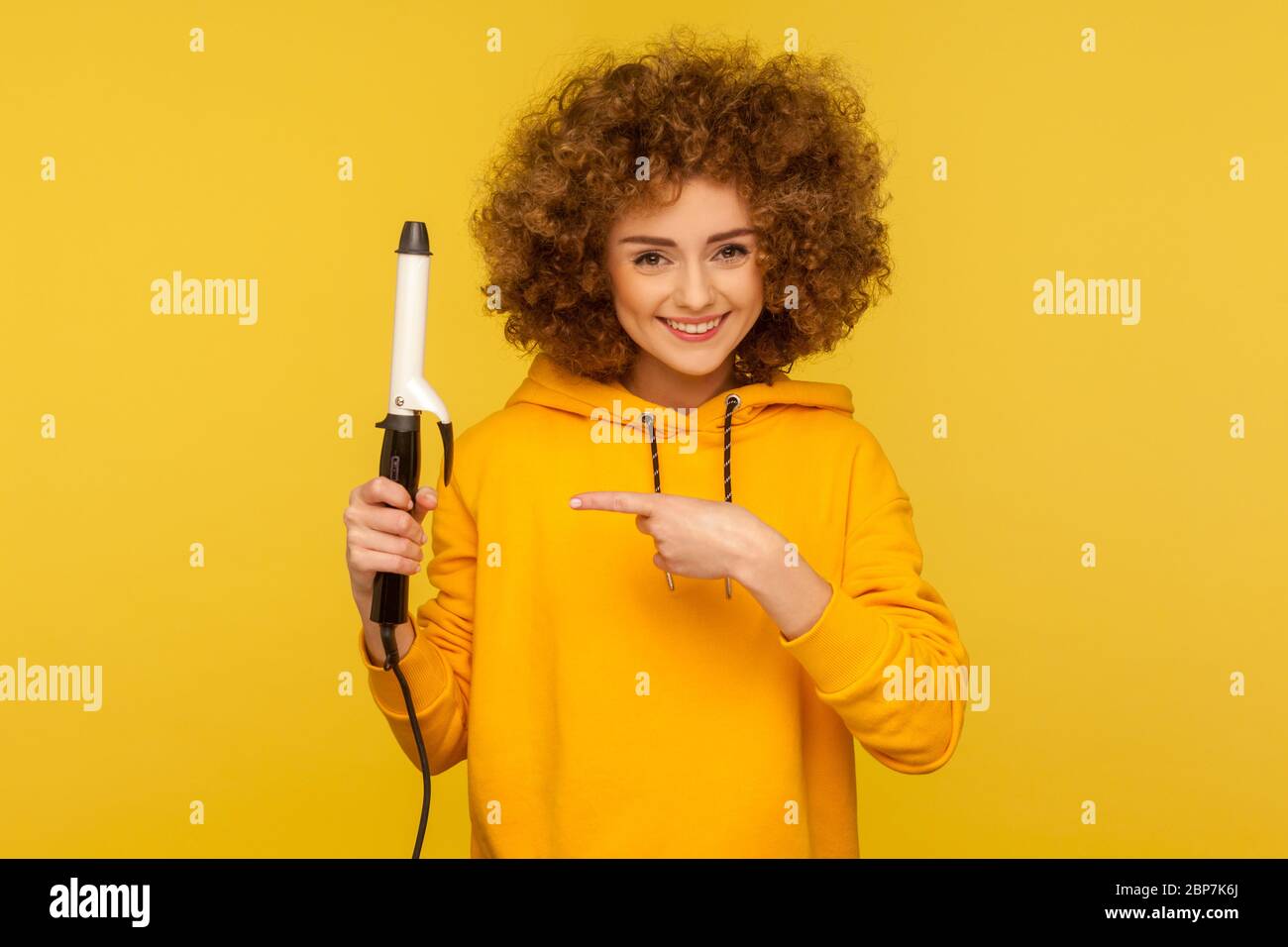 Happy fancy hipster woman in hoodie with perfect afro hairdo showing iron curler, professional curling tongs, beauty care concept and hairstyling. ind Stock Photo