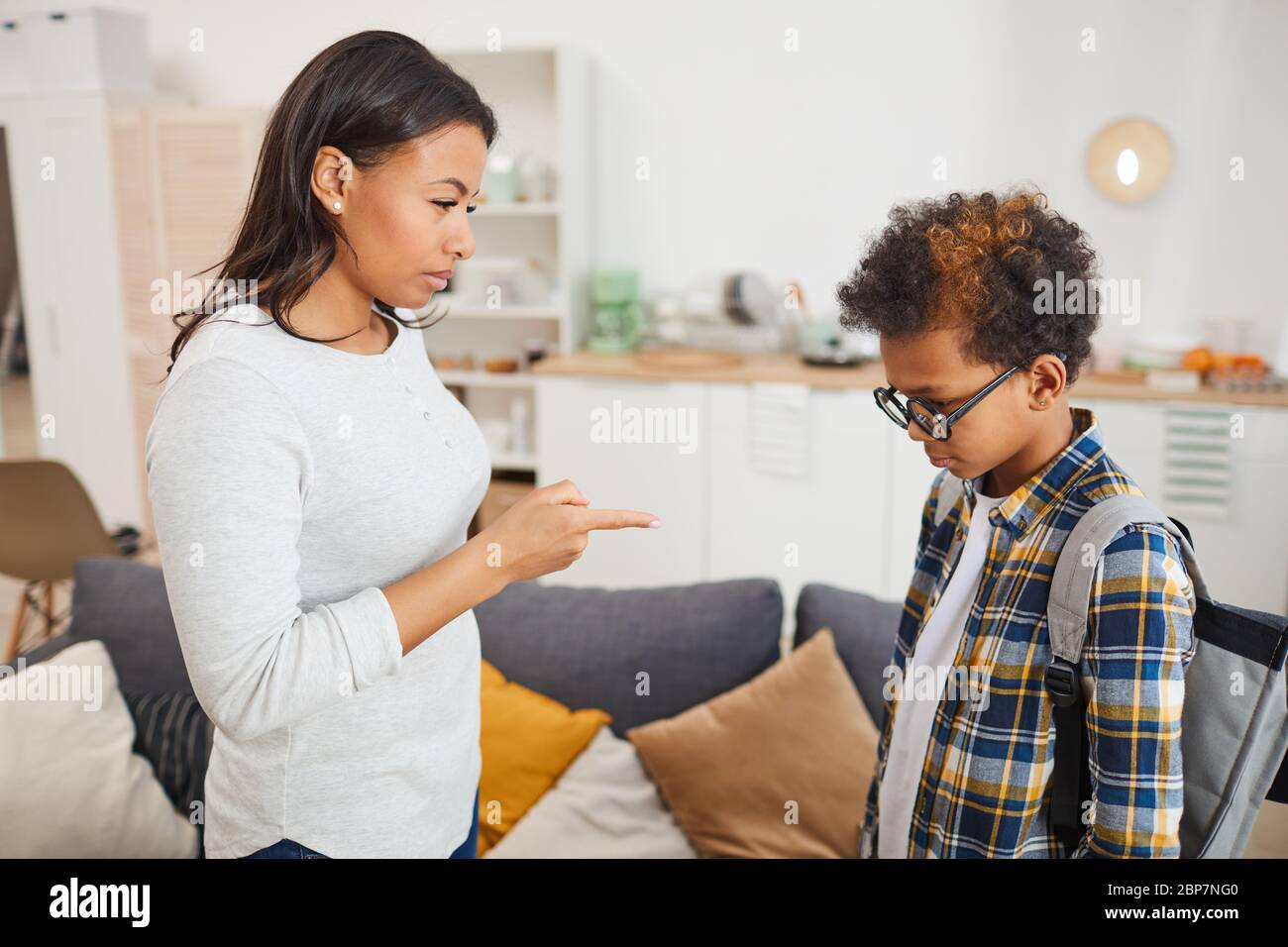 Side view portrait of young African-American woman scolding son for failing in school while standing in modern apartment interior Stock Photo