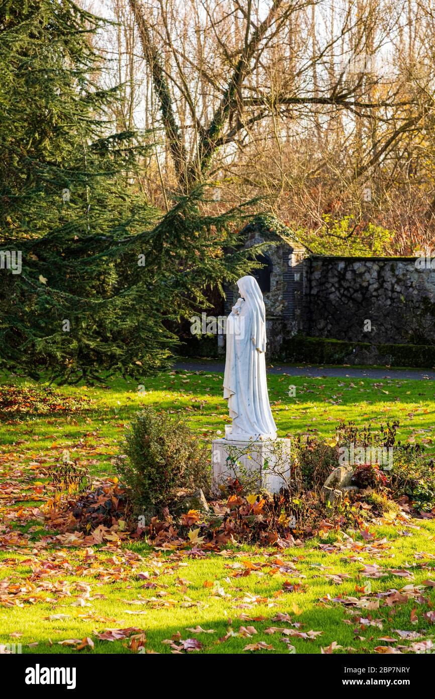 A statue in the Rosary Walk at Aylesford Priory of Our Lady Mary amongst the autumn leaves on a sunny winters day, Kent, UK Stock Photo