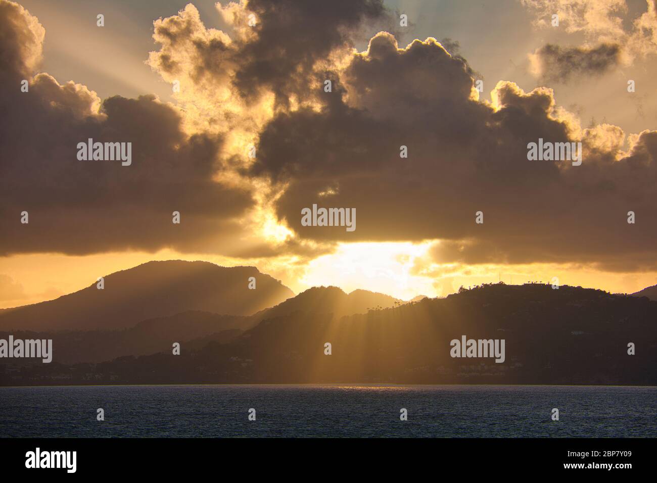 Sunrise over the west coast of St Lucia, the Caribbean, West Indies, with hills in silhouette and bright sun's rays against dramatic dark clouds Stock Photo