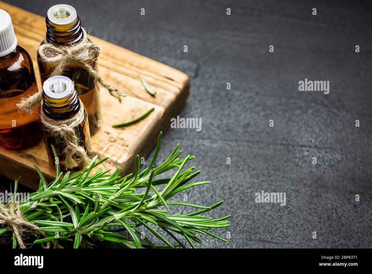 Rosemary herb branches and bottles of rosemary essential oil on black