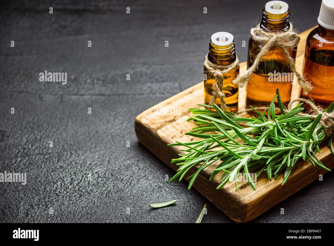Rosemary herb branches and bottles of rosemary essential oil on black