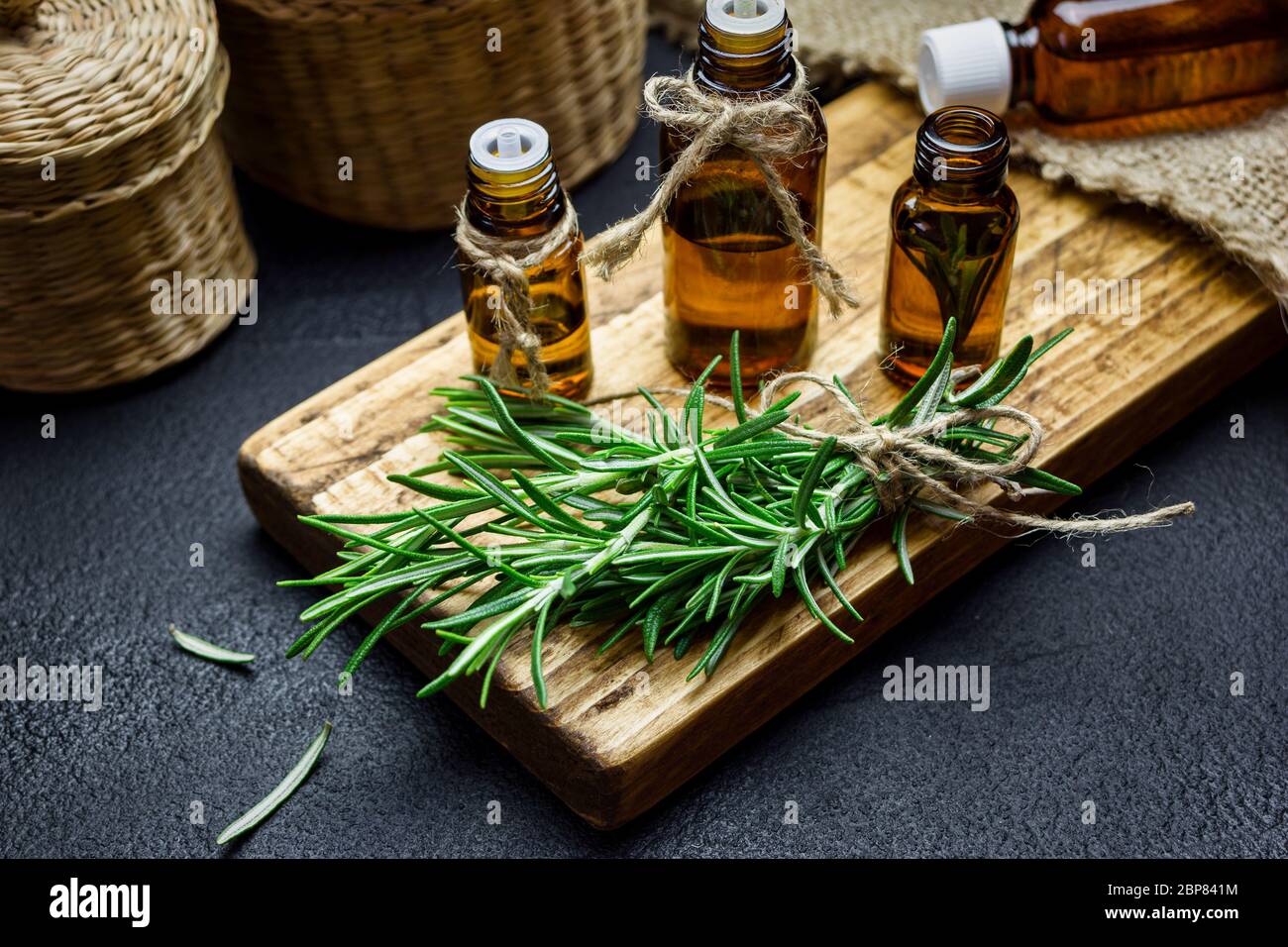 Rosemary herb branches and bottles of rosemary essential oil on black