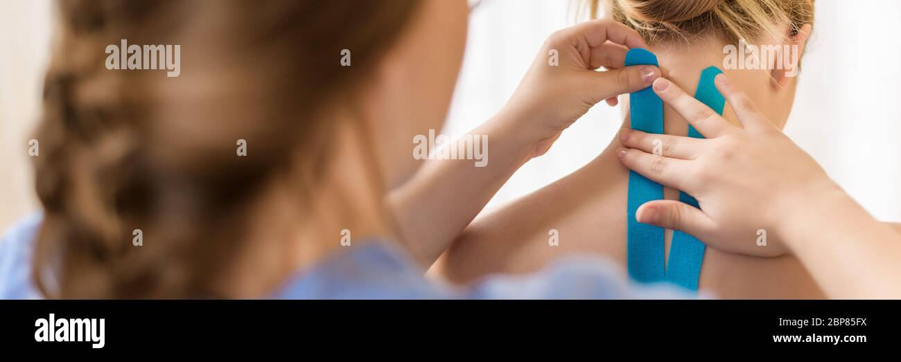 Female physiotherapist applying kinesio tape on patient's neck. Kinesiology, physical therapy, rehabilitation concept. Over the shoulder view banner. Stock Photo