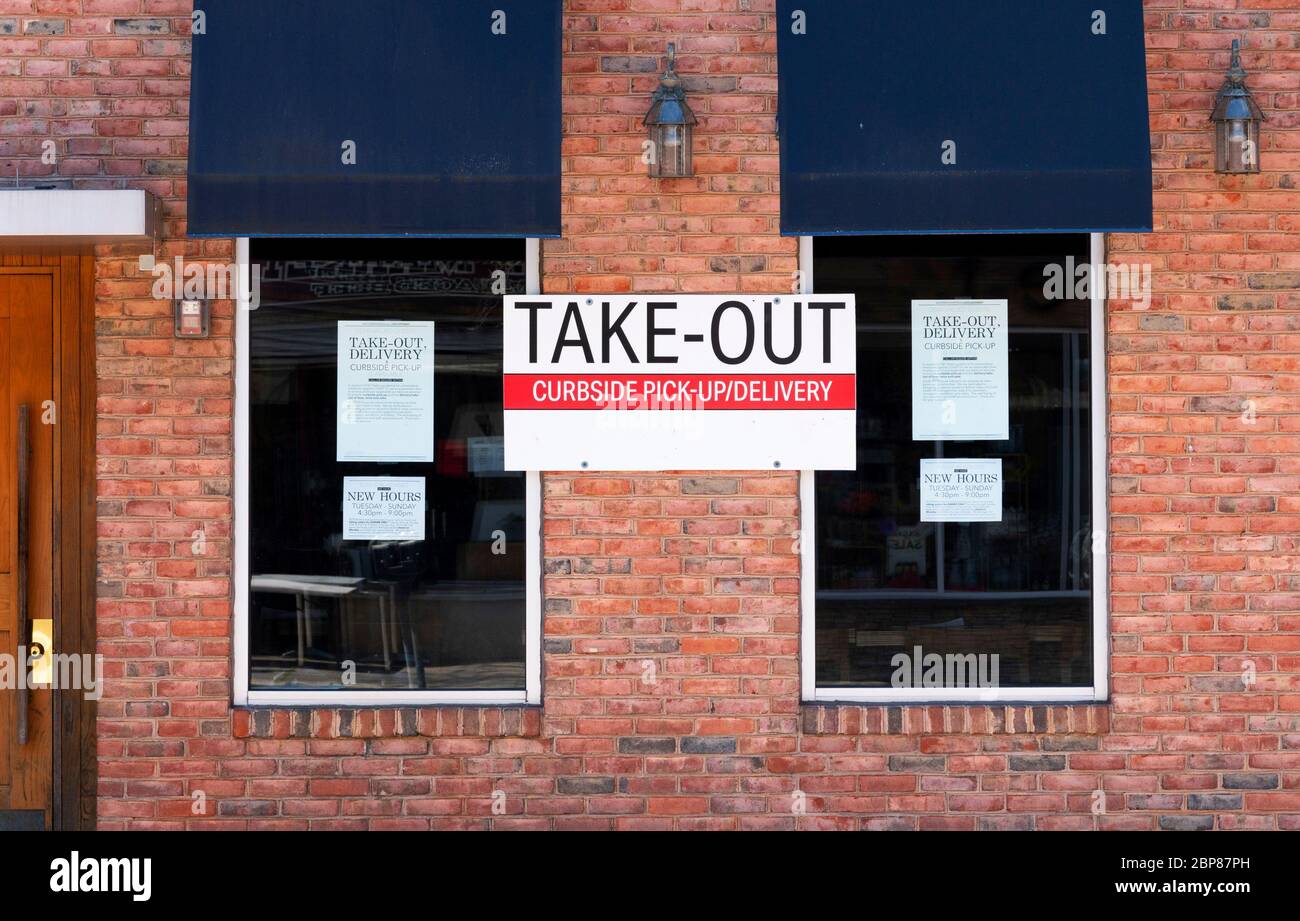 Take out curbside pick up or delivery only sign posted on the brick wall of a restaurant between its two windows with blue awnings due to coronavirus Stock Photo