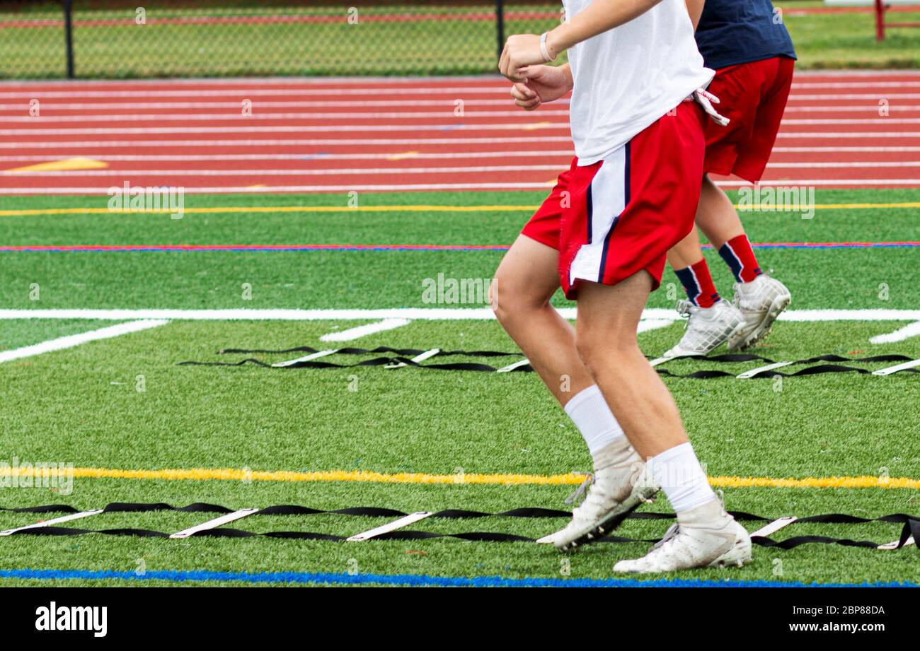 Two high school boys are running ladder drills on the turf during football summer camp. Stock Photo