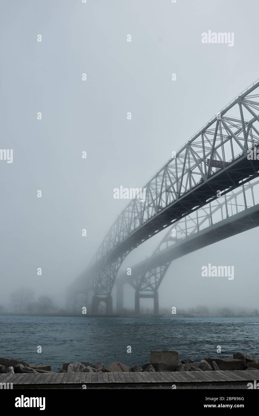 Fog surrounding twin span of bridges over river. Path leading to unknown future of coming out of the mist. Stock Photo