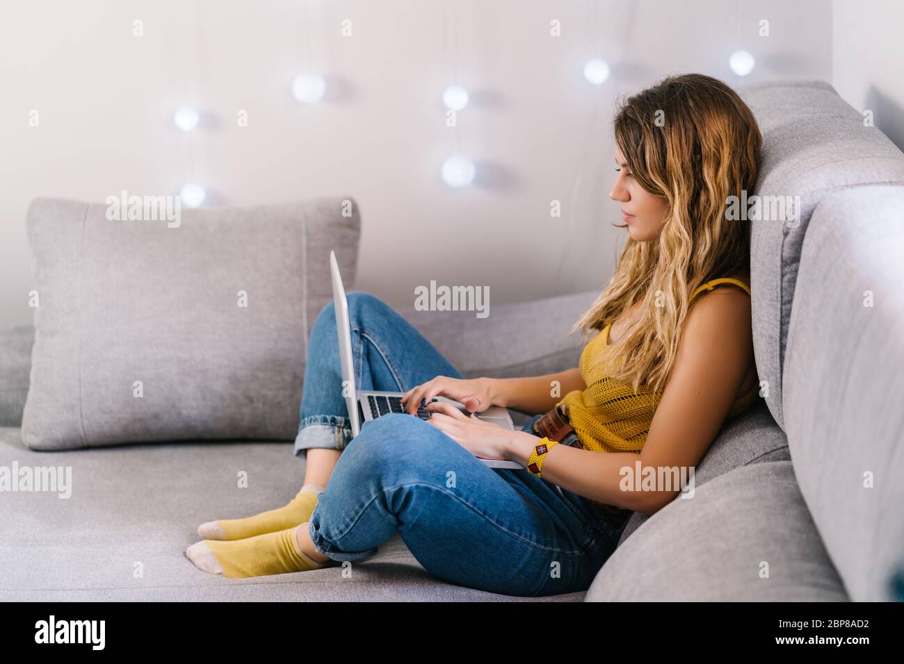 Blonde woman working at home with laptop sitting on sofa at home Stock ...