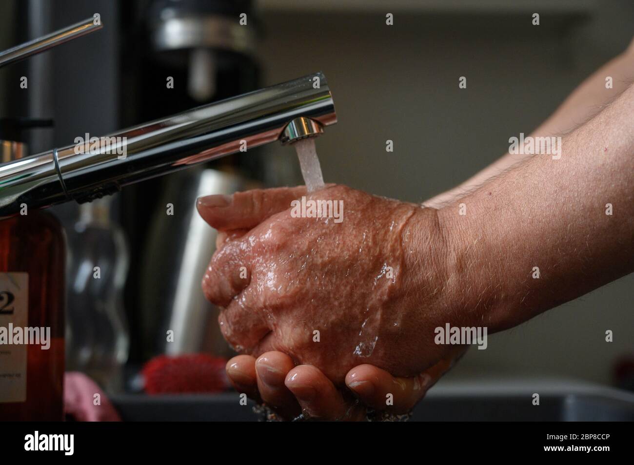 Man washing his hands under running water from the faucet in a hand basin or sink in a close up view conceptual of hygiene awareness for Covid-19 Stock Photo