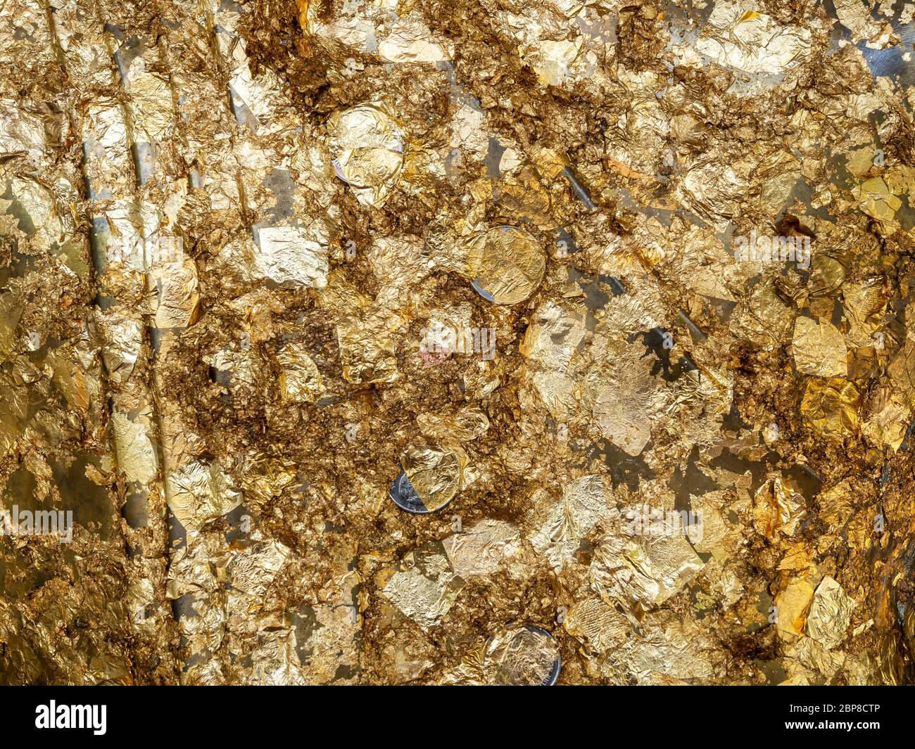 Shiny gold leaf with coins background.  Gold leaf texture on the back of a buddha statue placed by believer buddhists. Stock Photo