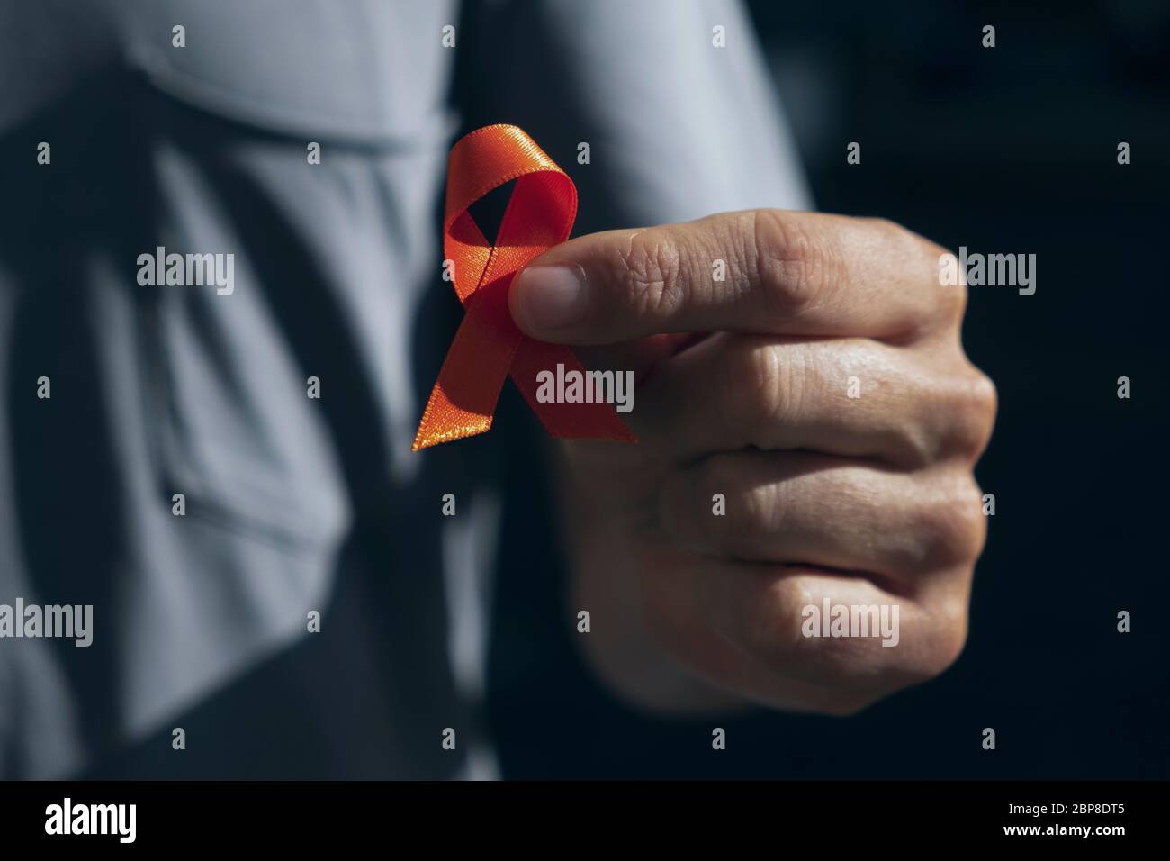 closeup of a young caucasian man with an orange ribbon in his hand, in support of people affected by multiple sclerosis Stock Photo