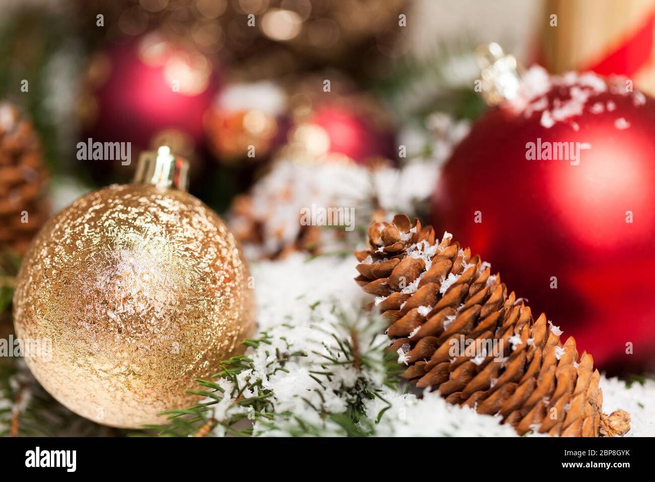 rote Weihnachtskugeln zwischen Zapfen und Tannenzweigen mit Schnee bedeckt als Macro Detail Stock Photo