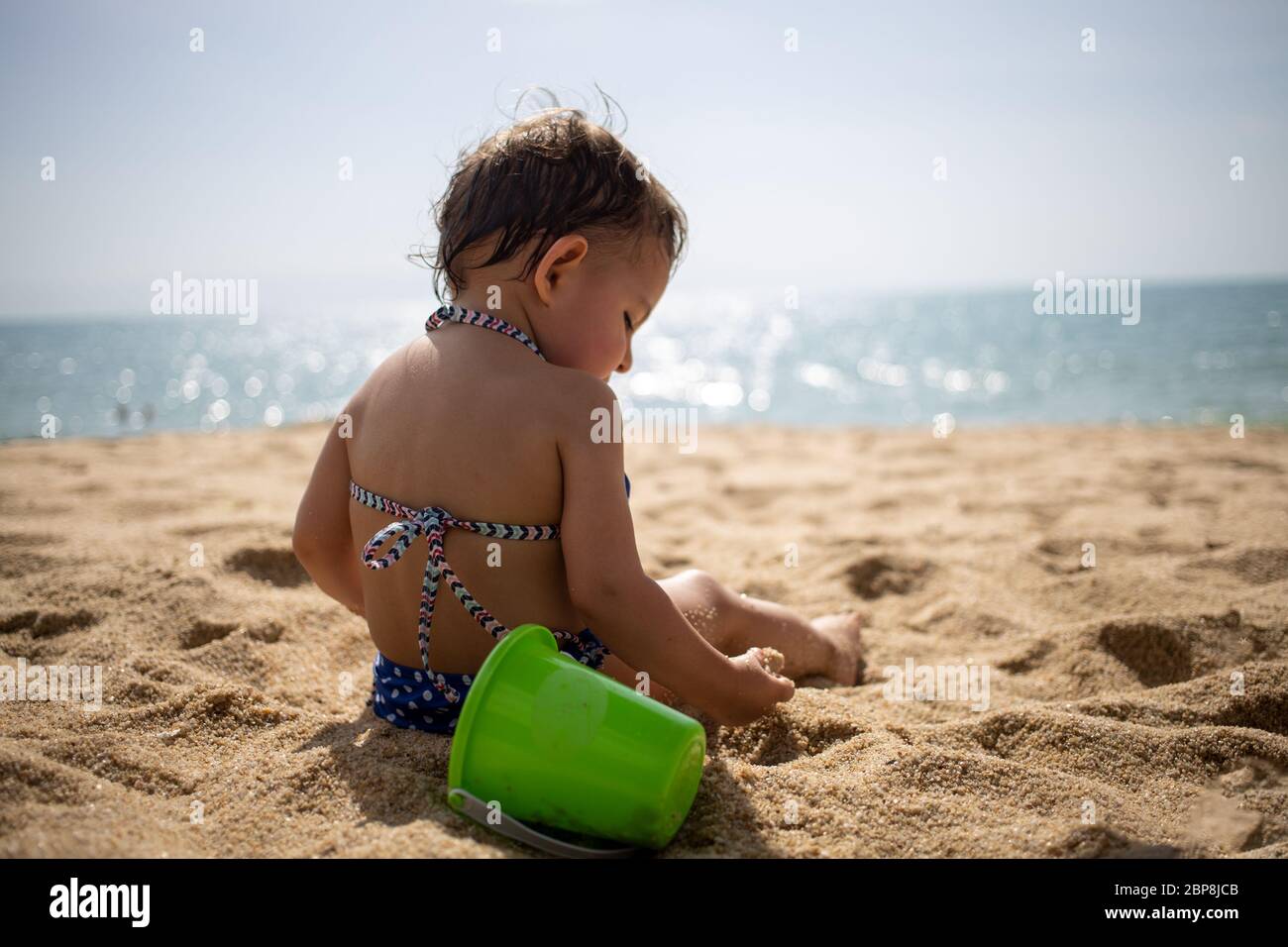 little cute toddler girl in a blue swimsuit on a sandy beach is studying  the sand against the background of sea waves on a warm sunny day Stock  Photo - Alamy