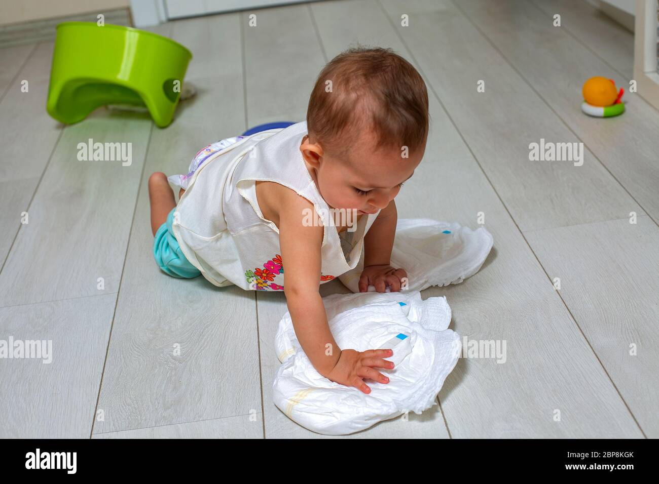 a little cute baby plays with clean new diapers on rhe whit floor. in the background a chamber pot ans toys in blur. .The concept of learning to use Stock Photo