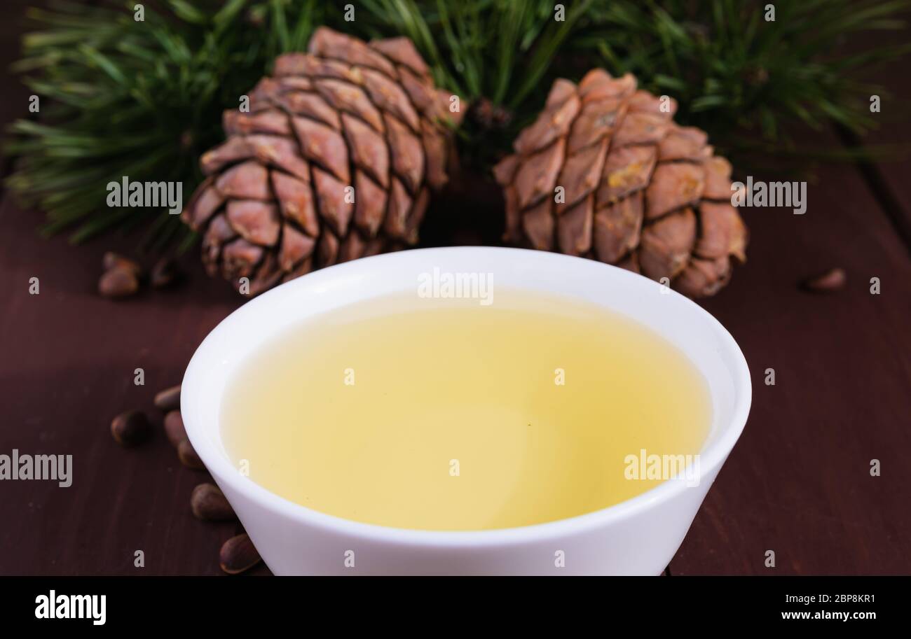 Cedar oil in a glass bottle and cedar cones with nuts on a old wooden table. Stock Photo