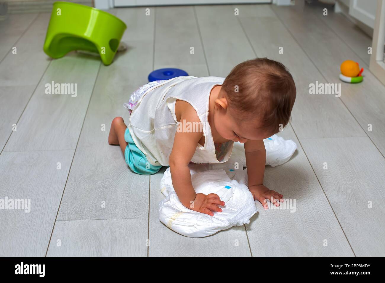 potty training concept. A cute little baby in a room on the bright floor plays with a diaper and an inverted green pot. soft focus Stock Photo