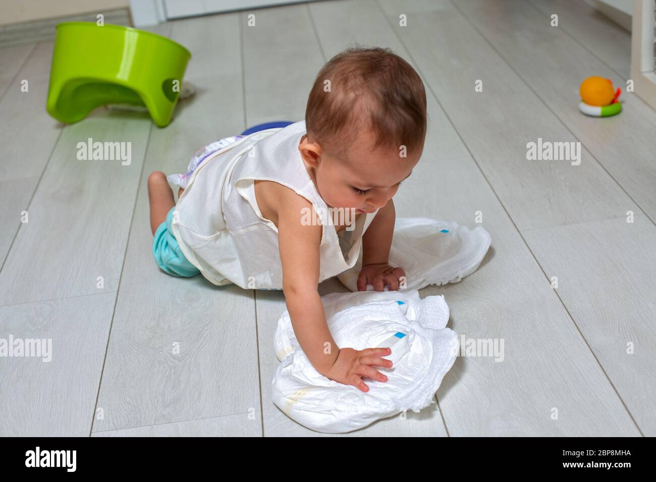 potty training concept. A cute little baby in a room on the bright floor plays with a diaper and an inverted green pot. soft focus Stock Photo