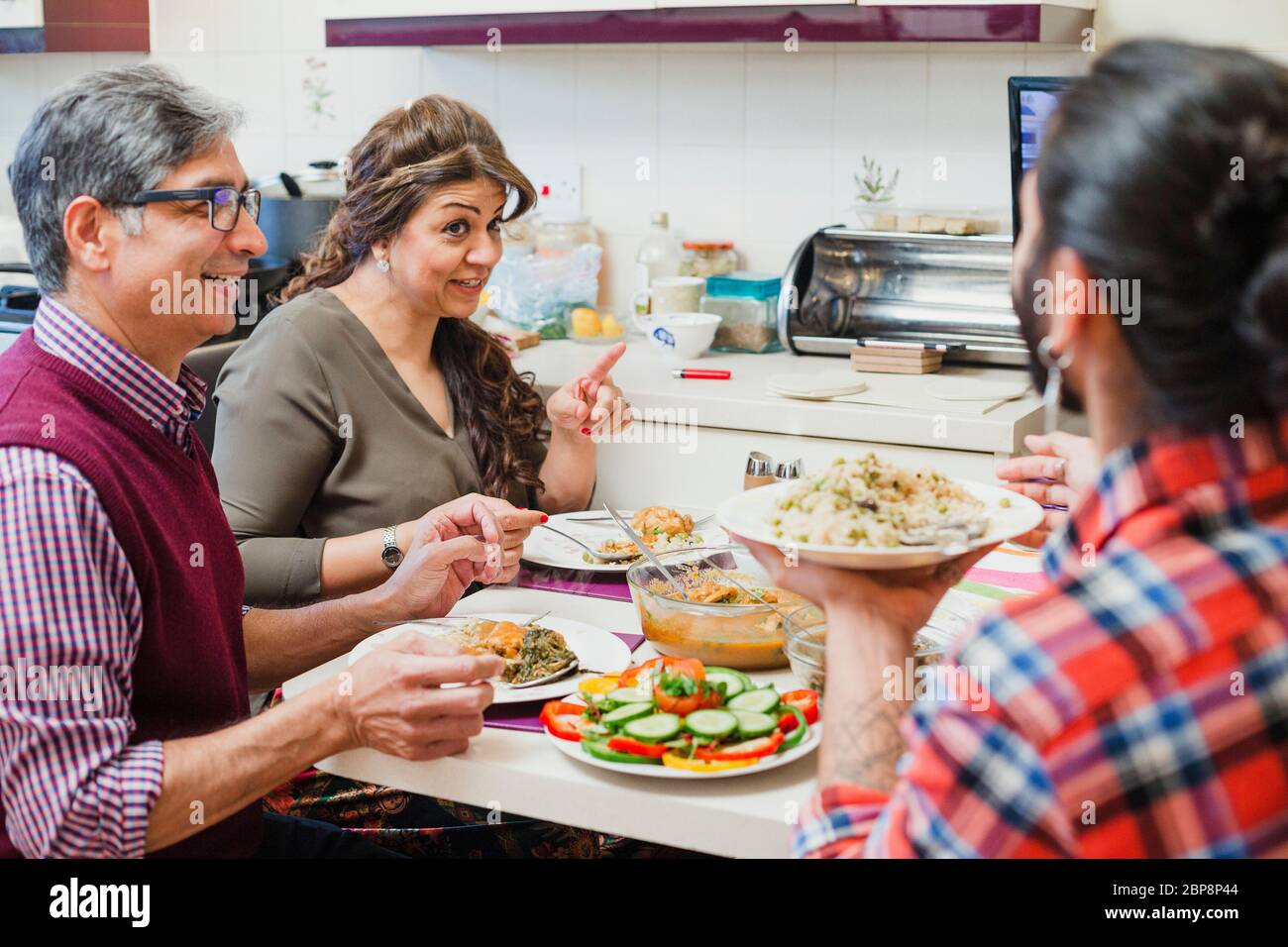 Family of three are enjoying a dinner together at home. They are talking while eating homemade curry and salad. Stock Photo