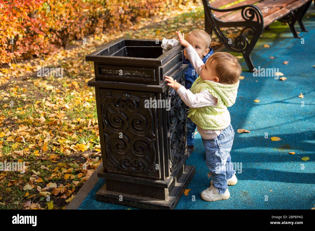 future ecology concept. two little cute babies are standing near the black street container in the park and throwing garbage there. another kid comes Stock Photo