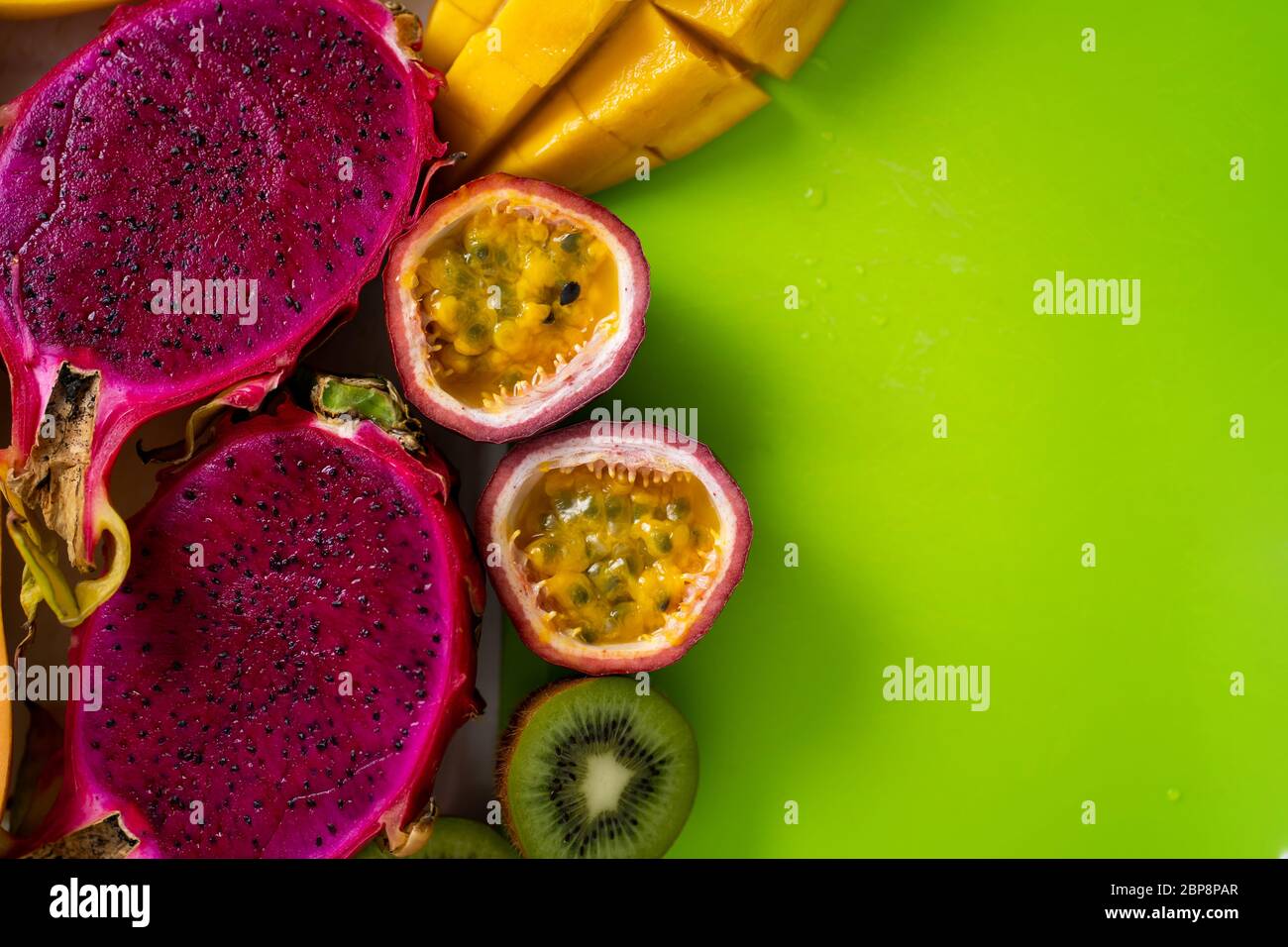 Closeup of sliced tropical exotic fruits on on green cutting board. Top view. Copy space for your text. Fresh mango, dragon fruit, kiwi, maracuja, pap Stock Photo