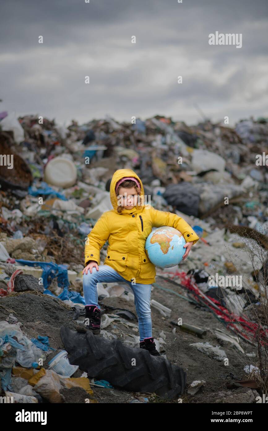 Small child holding globe on landfill, environmental pollution concept. Stock Photo