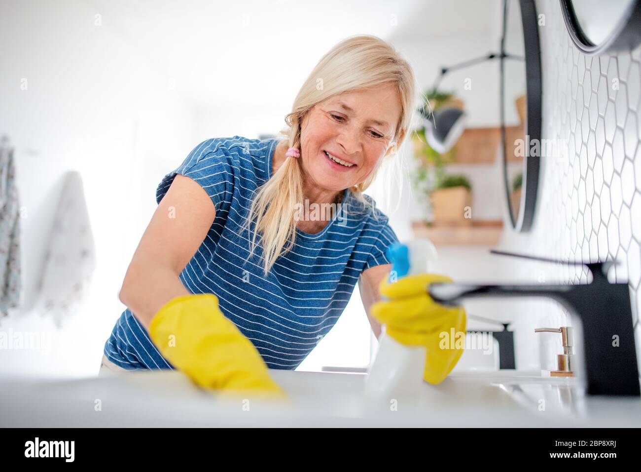 Senior woman with gloves cleaning bathroom indoors at home. Stock Photo