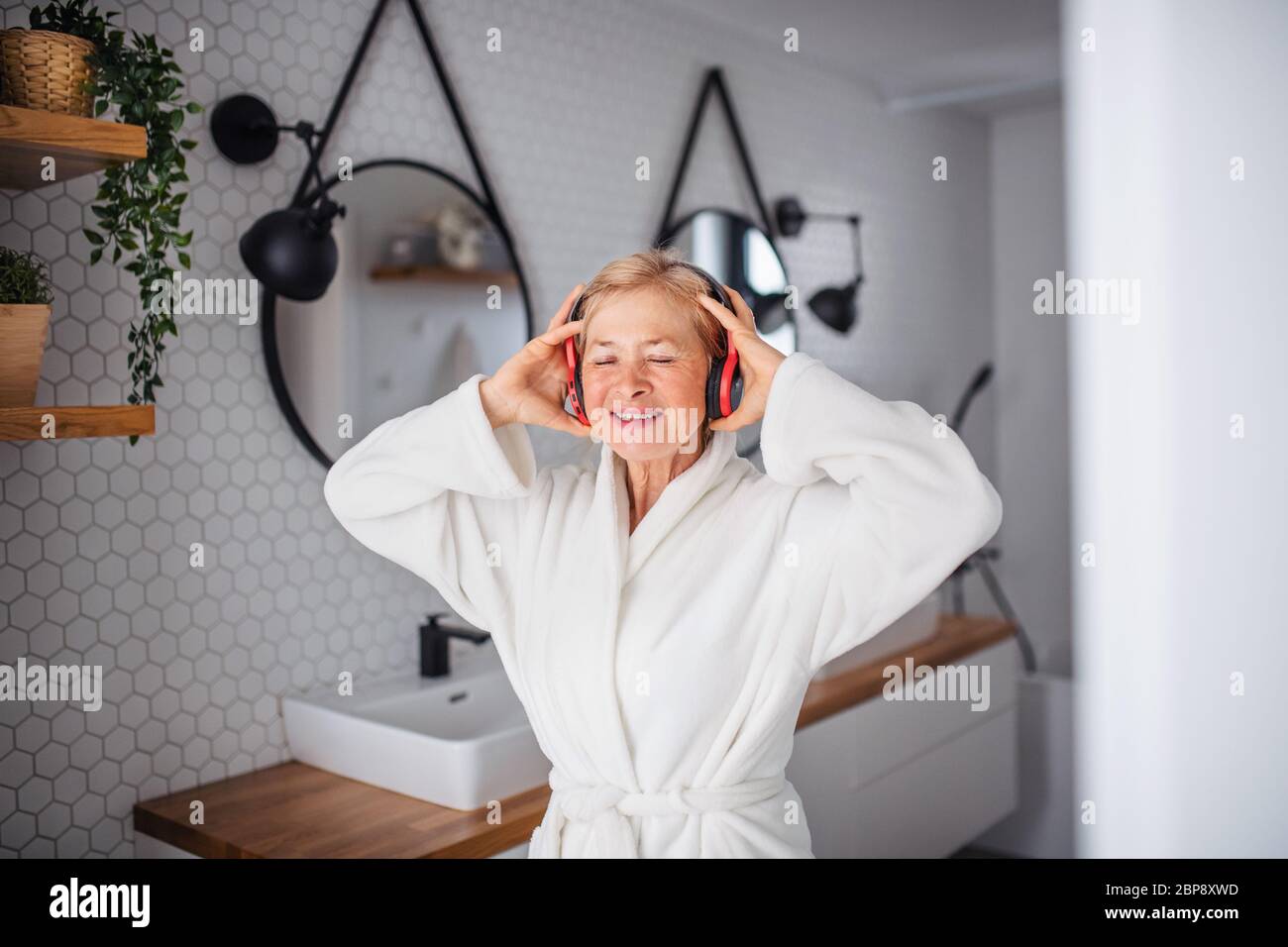 Portrait of senior woman with headphones and bathrobe indoors at home. Stock Photo